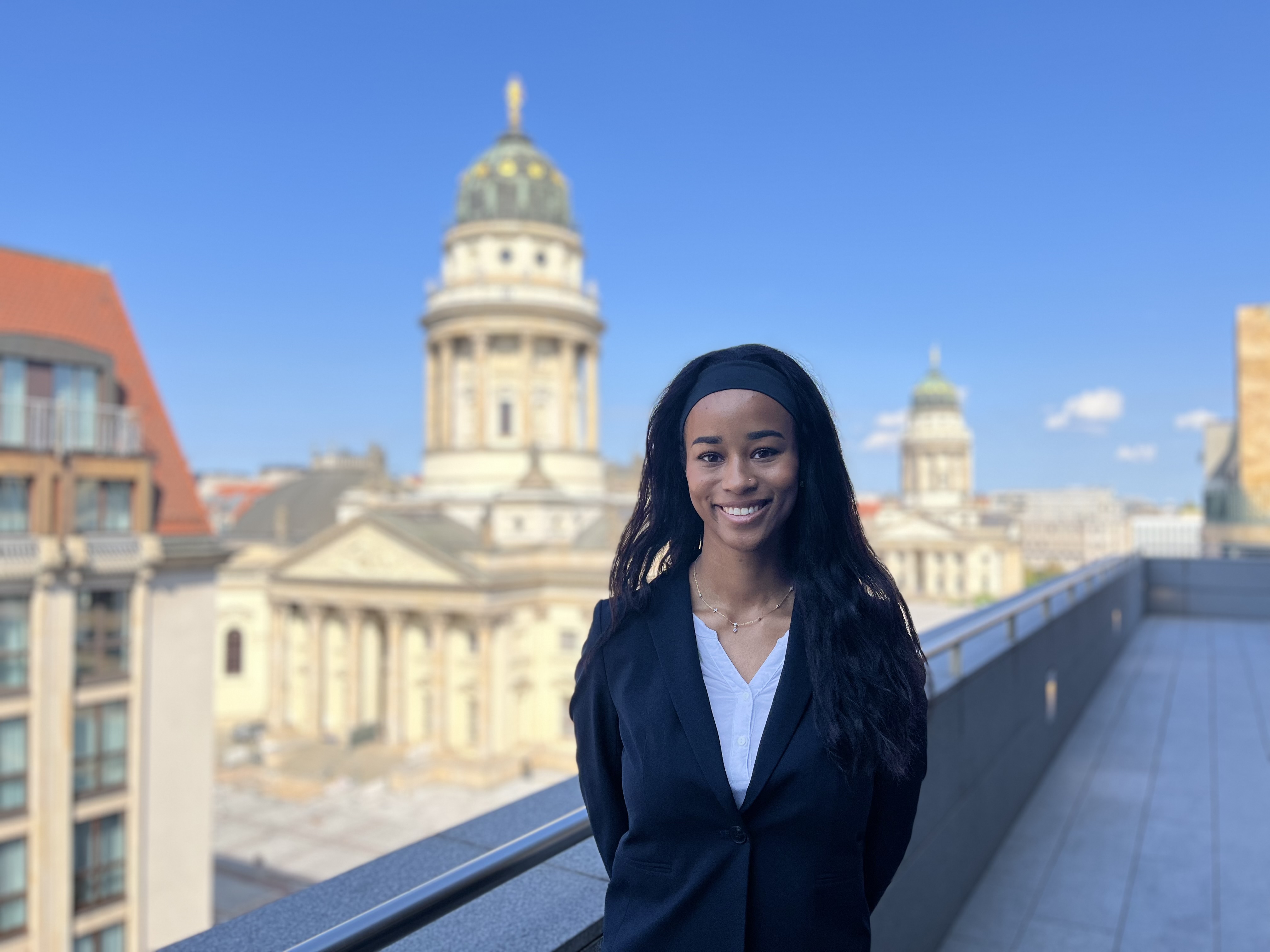 Foto showing a young woman, Lea Passo, who has been a participant of the Dentons Summer Internship program Meet Dentons standing on a balcony with the Gandarmenmarkt in the background. 